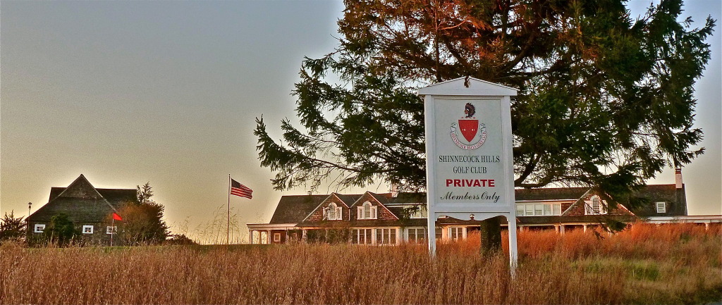 The Shinnecock Hills Golf Club entrance sign at dusk with the clubhouse behind