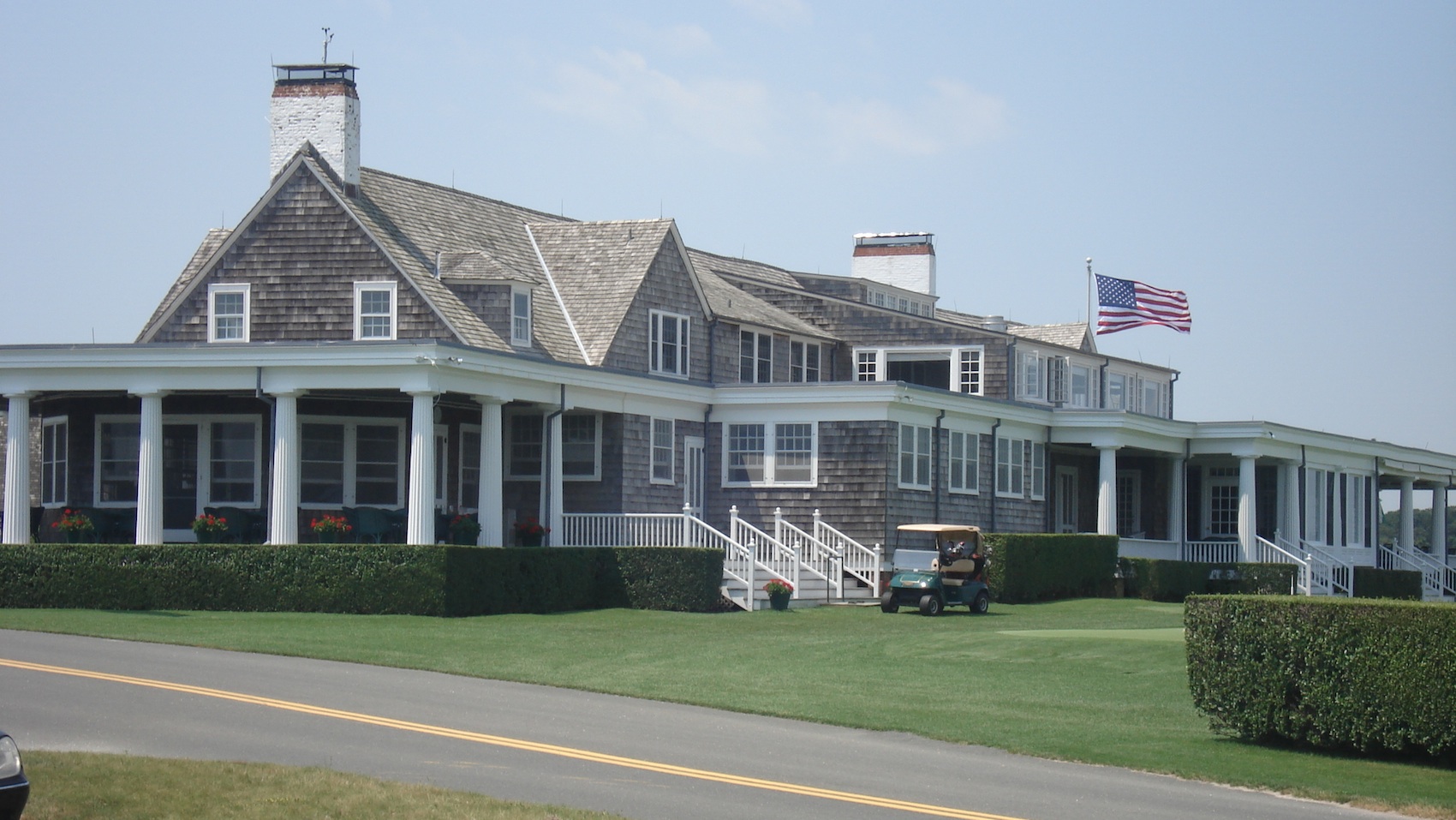 The Shinnecock Hills clubhouse today, shingled with a white columned veranda and an American flag