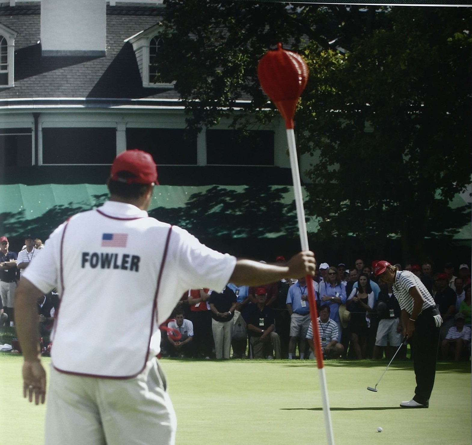 A red Merion wicker basket flagstick held by a caddie during a modern championship at Merion Golf Club
